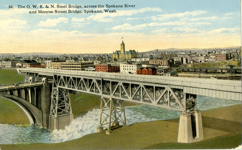A view of the Oregon-Washington Railroad and Navigation Company bridge and the Monroe Street Bridge crossing the Spokane River, with the city in the background.