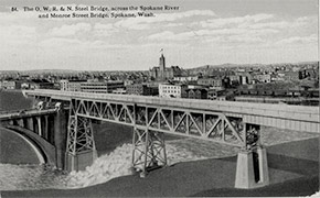 A view of the Oregon-Washington Railroad and Navigation Company bridge and the Monroe Street Bridge crossing the Spokane River, with the city in the background.